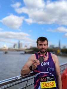 Dan standing by river Thames with London Marathon 2022 medal