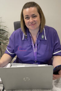 Nurse in purple uniform in front of a laptop with a phone in her hand 