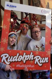 Three females wearing antler headbands post with Rudolph Run frame